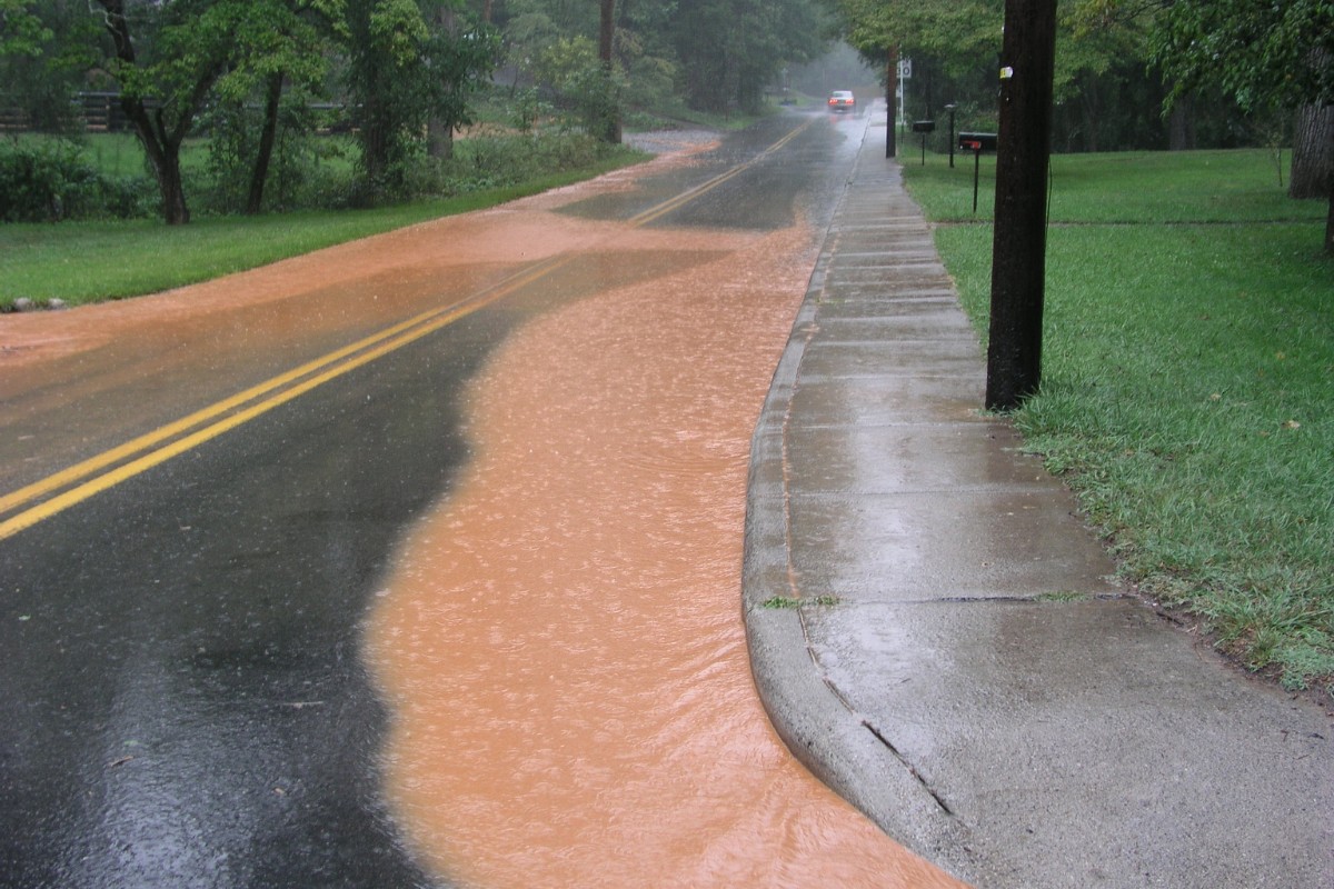 Brown, muddy water running along the edge of a South Florida street after heavy rain.